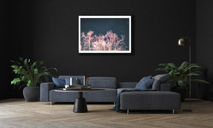Framed photo of long exposure winter storm photo with swaying trees and starry sky, reddish light, black living room wall.