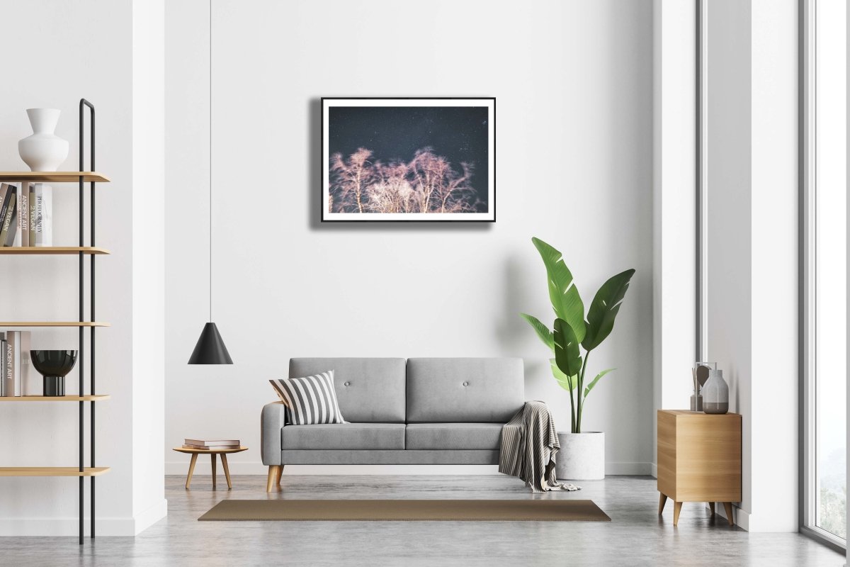 Framed photo of long exposure winter storm photo with swaying trees and starry sky, reddish light, white living room wall.