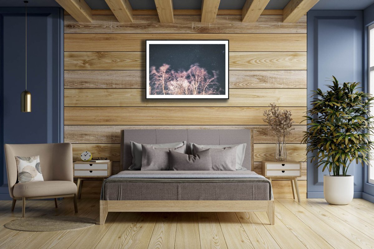 Framed photo of long exposure winter storm photo with swaying trees and starry sky, reddish light, wooden bedroom wall.