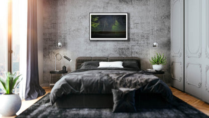 Fine art print of nocturnal forest and lakeside, black-framed on gray stone wall above bed in bedroom.