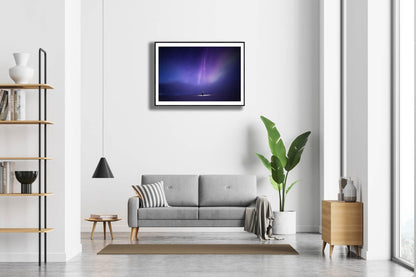 Framed photo of person under aurora borealis and fainting clouds, white living room wall.