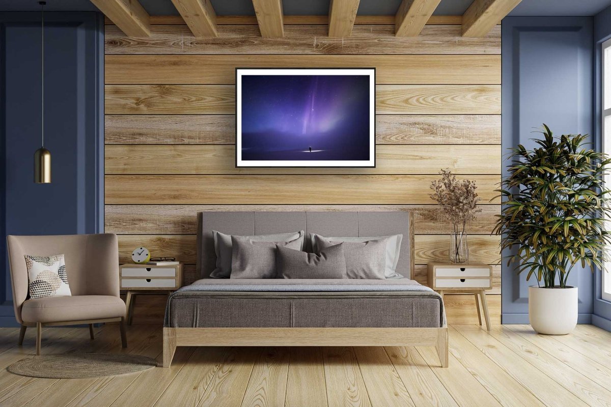 Framed photo of person under aurora borealis and fainting clouds, wooden bedroom wall.