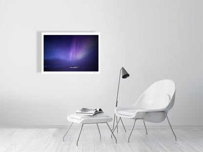 Photo of person under aurora borealis and fainting clouds, white living room wall.